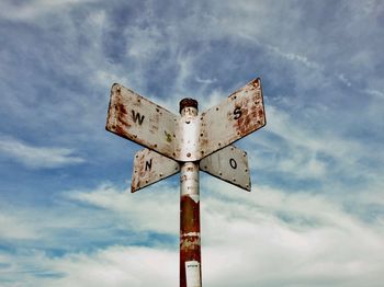 Low angle view of rusty information sign against sky