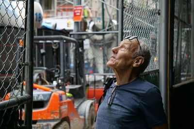 Thoughtful senior man standing by fence in city