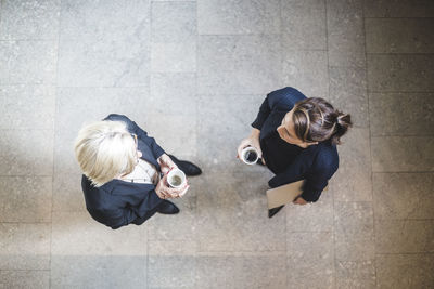High angle view of senior businesswoman standing with coworker while drinking coffee in office
