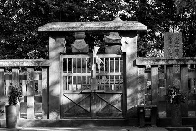 Woman sitting by built structure against trees