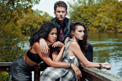 Portrait of young couple sitting on lake against trees