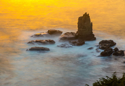 Rocks in sea against sky during sunset