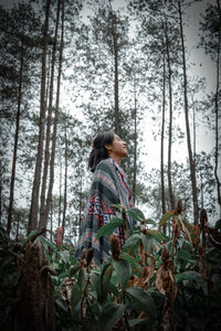 Low angle view of mid adult woman standing amidst plants in forest