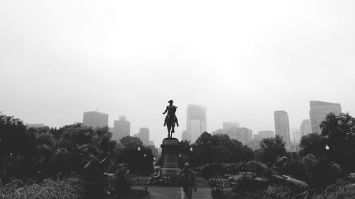 Man walking by george washington monument at garden in city against clear sky