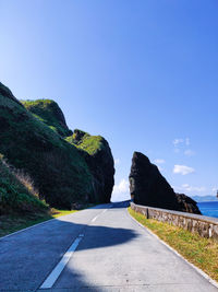 Empty road by mountain against clear blue sky