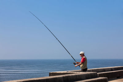 Man fishing by sea against sky