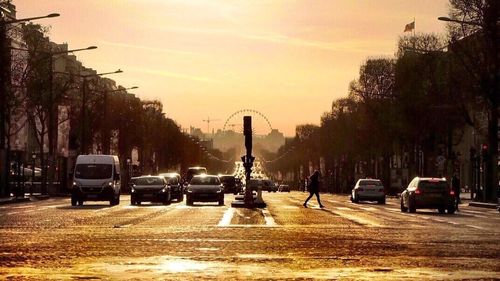 Cars on street in city against sky at sunset