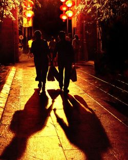 Rear view of silhouette couple walking on illuminated road