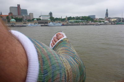 Low section of man by river against buildings in city