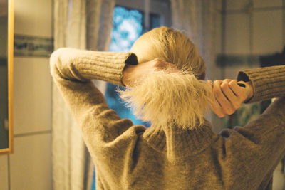 Rear view of woman brushing hair at home