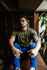 Portrait of young man sitting by plant indoors