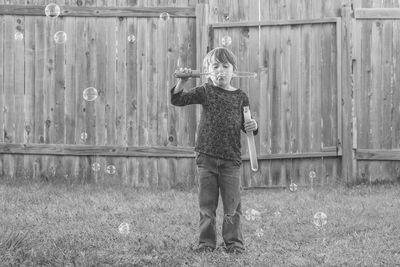 Full length of boy blowing bubbles while standing against fence