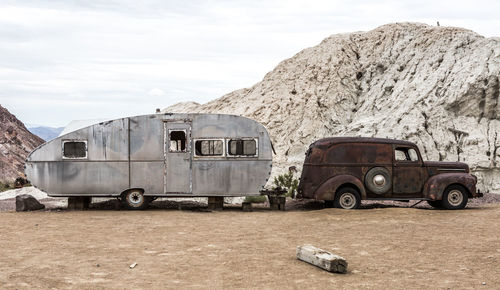 Abandoned vehicles by mountain against sky