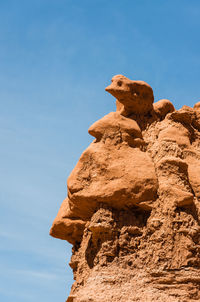 Low angle view of rock on cliff against blue sky