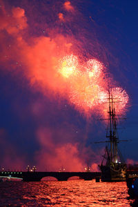 Sailboat sailing in river against fireworks at dusk