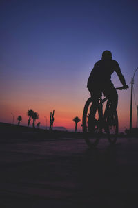 Silhouette man riding bicycle against sky during sunset