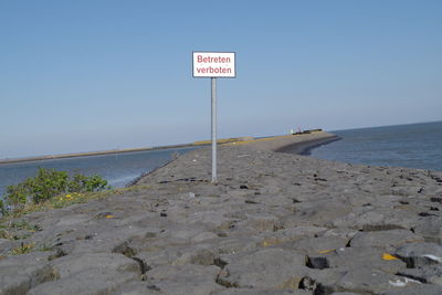 Information sign on beach against clear sky