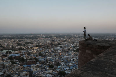 Tourists looking at cityscape against sky during sunset