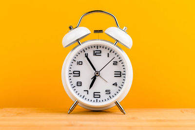 Close-up of clock on table against yellow background