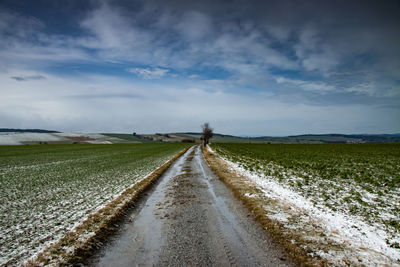 Surface level of road amidst field against sky