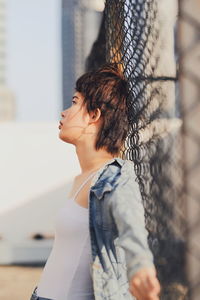 Woman looking away while leaning on chainlink fence