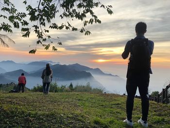 Rear view of men standing on land against sky during sunset