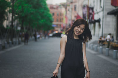 Smiling young woman standing against buildings in city