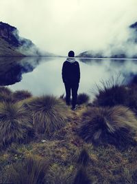 Rear view of man standing by lake against sky