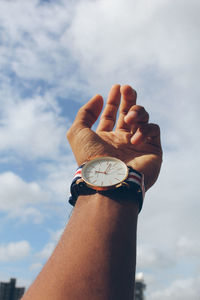 Cropped hand of man wearing wristwatch against sky
