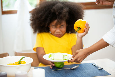 Midsection of woman giving fruits in plate to daughter sitting at table