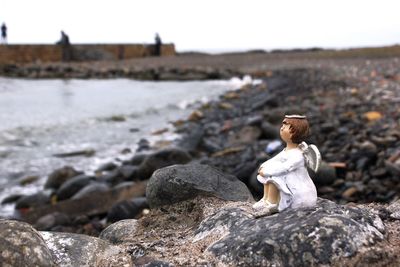 Woman sitting on rock by river against sky