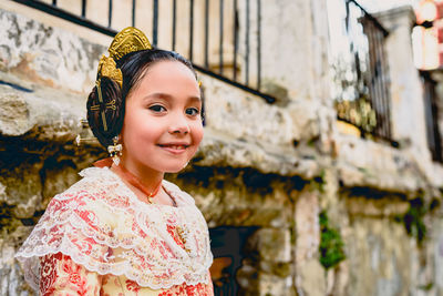 Portrait of smiling girl in pink dress standing against wall