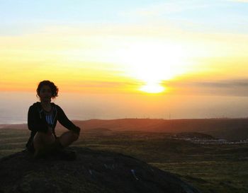 Portrait of man sitting on landscape against sky during sunset