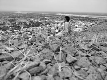 Rear view of man sitting on land against sky