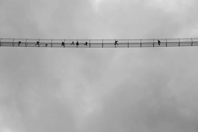 Low angle view of birds perching on cable against sky