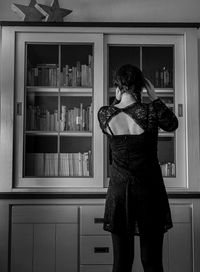 Rear view of woman standing against shelves at home