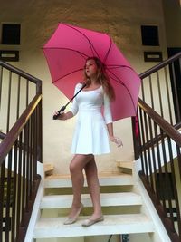 Full length of woman holding umbrella while standing on staircase by railing