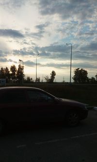 Street by trees against sky at sunset