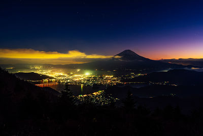 Aerial view of illuminated city and silhouette mountains against sky at night