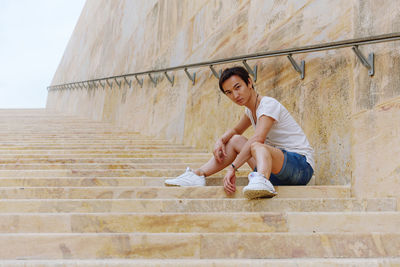 Young man sitting on staircase against wall