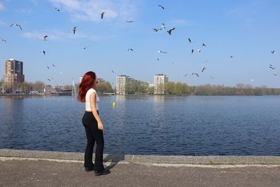 Rear view of woman standing by lake against sky