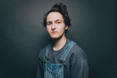 Portrait of trendy young man wearing bib overalls over colored background