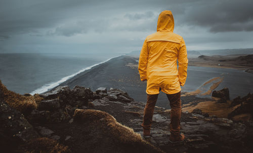 Rear view of man standing on rock by sea against sky