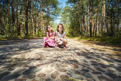 Full length portrait of cute girl crouching on footpath