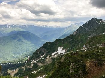 Scenic view of mountains against cloudy sky with a bridge and two people walking towards each other