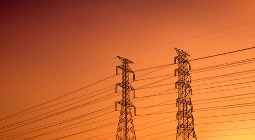 Low angle view of electricity pylon against orange sky. high voltage electric pole.