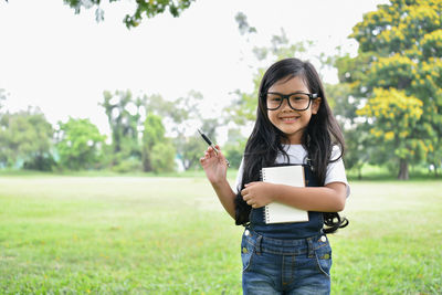 Portrait of smiling girl holding book while standing at park