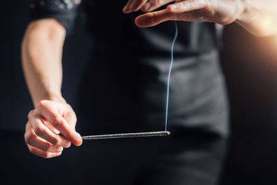 Hands holding a burning incense stick, black background