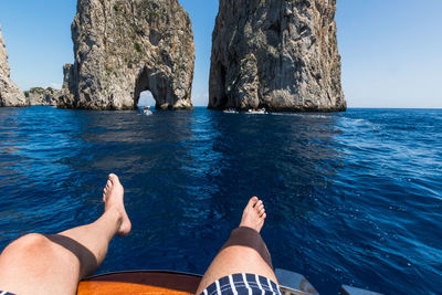 Low section of man relaxing on rock by sea