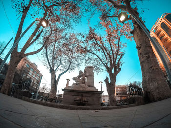 Low angle view of statue amidst trees and buildings against sky